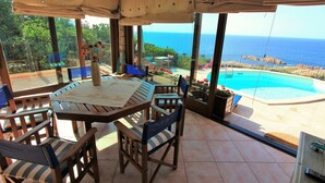 A covered patio with a table and chairs, overlooking a swimming pool and the sea. - Charming retreat with panoramic private pool, 300m from the sea (Trinità d'Agultu e Vignola)