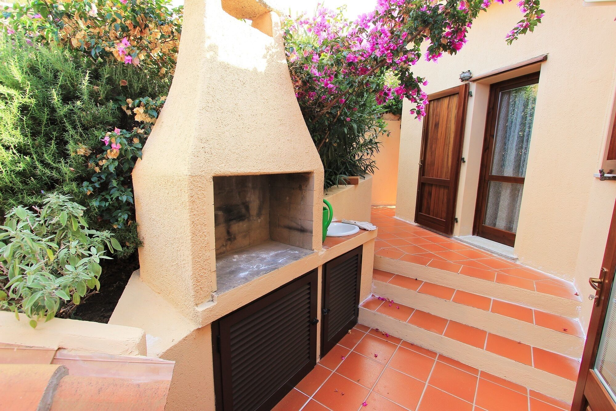 An outdoor kitchen area with a stone oven, surrounded by plants and a tiled patio.