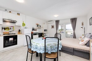 A modern kitchen with white cabinets, a dining table with chairs, and a balcony with a sofa.