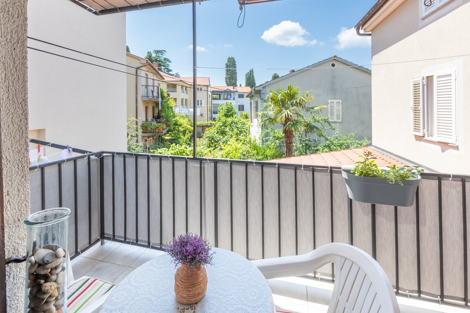 Een balkon met een tafel, stoelen, een hangende plant en een glazen pot met stenen.