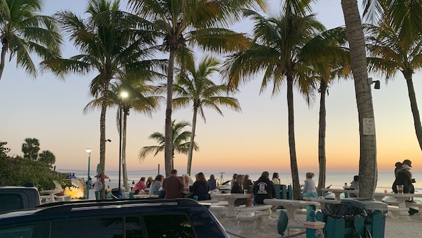 A beachside area with palm trees, picnic tables, and a car parked nearby. - Beach, Shelling, Water Sport, Restaurant Right Across The Street!  Paradise!! (Bonita Springs)