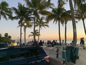 A beachside area with palm trees, picnic tables, and a car parked nearby. - Beach, Shelling, Water Sport, Restaurant Right Across The Street!  Paradise!! (Bonita Springs)