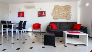 A modern living room with a black and white sofa, a red chair, a dining table with chairs, and a wall-mounted air conditioner. - Apartment Adria 1 on the island Krk (Malinska)