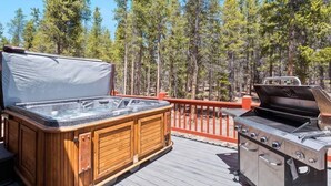 A hot tub and grill on a wooden deck with a forest backdrop. - Imogene Home — 4BR + Hot Tub, Sleeps 10, 15 min to Ski Cooper, Ping Pong Garage (Leadville)