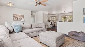 A spacious living room with a sectional sofa, ottoman, and a ceiling fan. - Imogene Home — 4BR + Hot Tub, Sleeps 10, 15 min to Ski Cooper, Ping Pong Garage (Leadville)