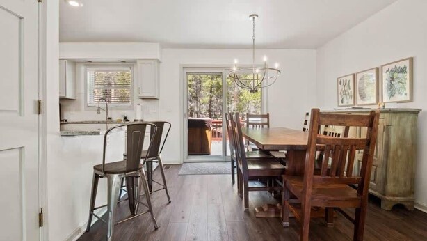 A dining area with a wooden table and chairs, a chandelier, and a view through a glass door to an outdoor space. - Imogene Home — 4BR + Hot Tub, Sleeps 10, 15 min to Ski Cooper, Ping Pong Garage (Leadville)