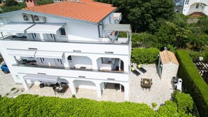 Um edifício branco de vários andares com telhado de telhas vermelhas, pátio com calçada de pedra e área de estar externa.