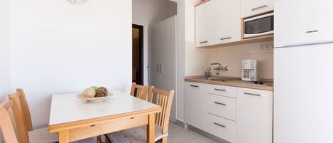 Una cocina moderna con muebles blancos, microondas, cafetera y una mesa de comedor con sillas.