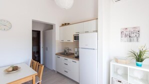 Eine moderne Küche mit weißen Schränken, einer Mikrowelle und einem Spülbecken. Es gibt einen Esstisch mit Stühlen und eine Uhr an der Wand.