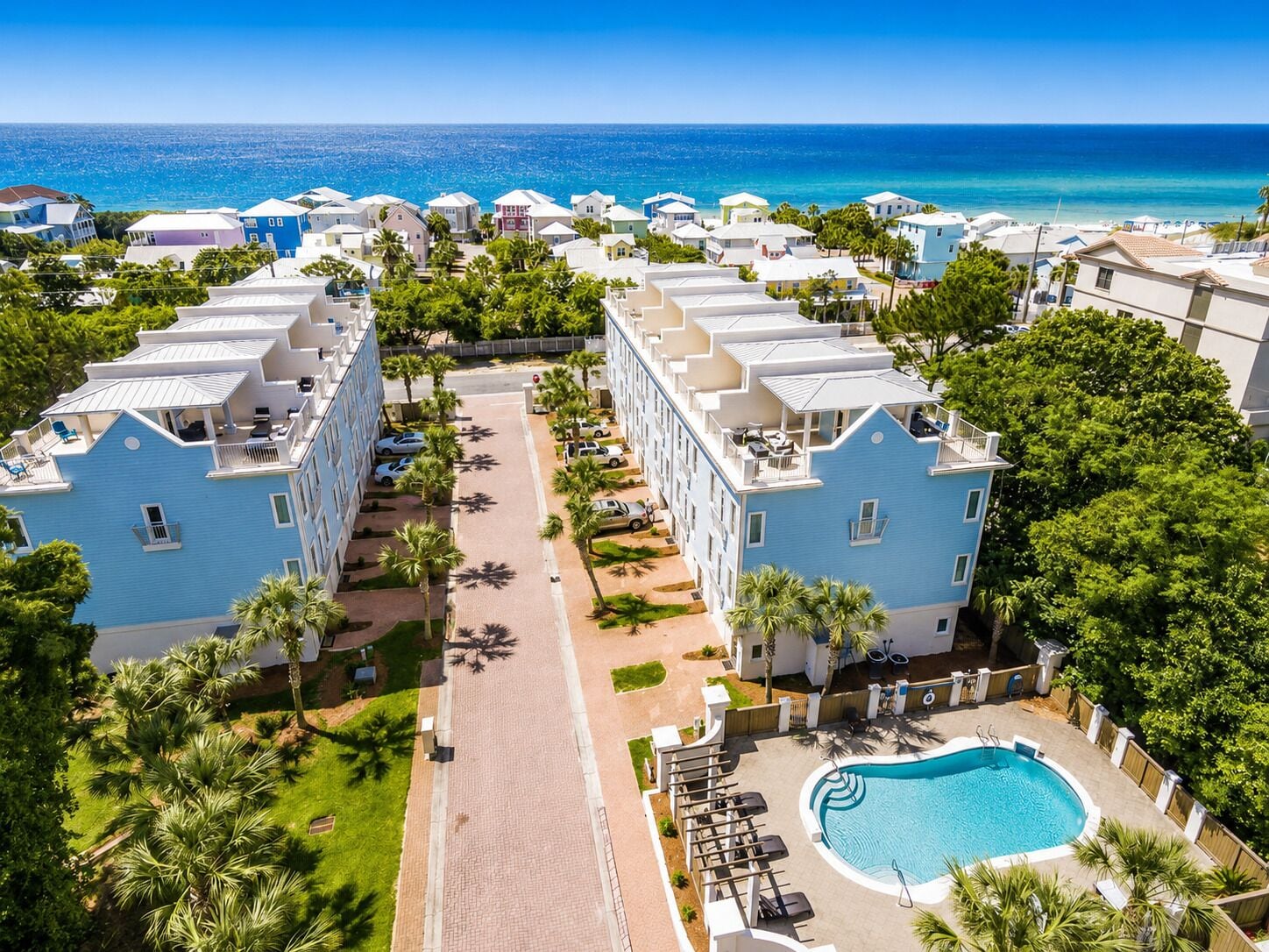 A resort with multiple-story buildings, a central pool, and a view of the ocean.