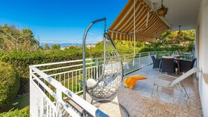 Un balcon agrémenté d’un fauteuil suspendu, d’une table avec des chaises, et offrant une vue sur la mer et la verdure.