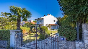 Une maison à deux étages, avec une façade blanche, un mur en pierre et un portail en métal.