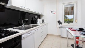 Une cuisine moderne avec des meubles blancs, un évier en acier inoxydable, un four à micro-ondes encastré et une cuisinière à gaz.