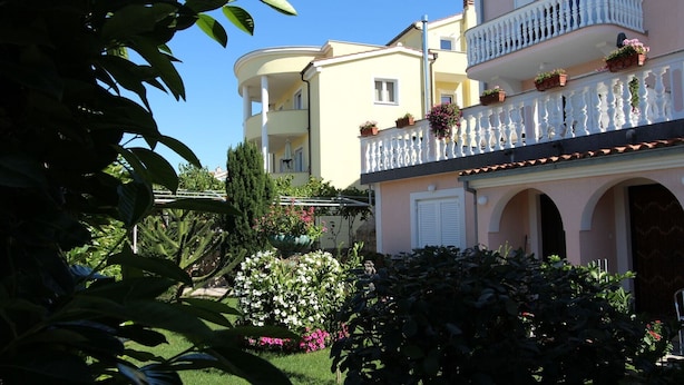 Un edificio de varios pisos con balcones, un jardín con diversas plantas y un cielo azul despejado.
