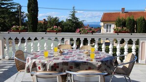 Un área de comedor al aire libre con una mesa preparada para cuatro personas, rodeada de balaustradas blancas y sillas de mimbre.