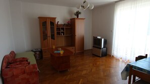 Un saló amb un paviment de fusta en relllaç, un armari de fusta amb portes de vidre, una televisió sobre un suport i una taula de dinar amb cadires.