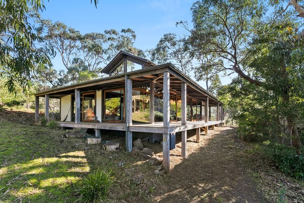 A wooden structure with a covered porch, surrounded by trees.