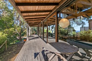 An outdoor wooden deck with a glass enclosure, wooden beams overhead, and a hanging light fixture.