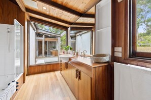 A modern bathroom with wooden cabinetry, a large window, and a view of the outdoors.