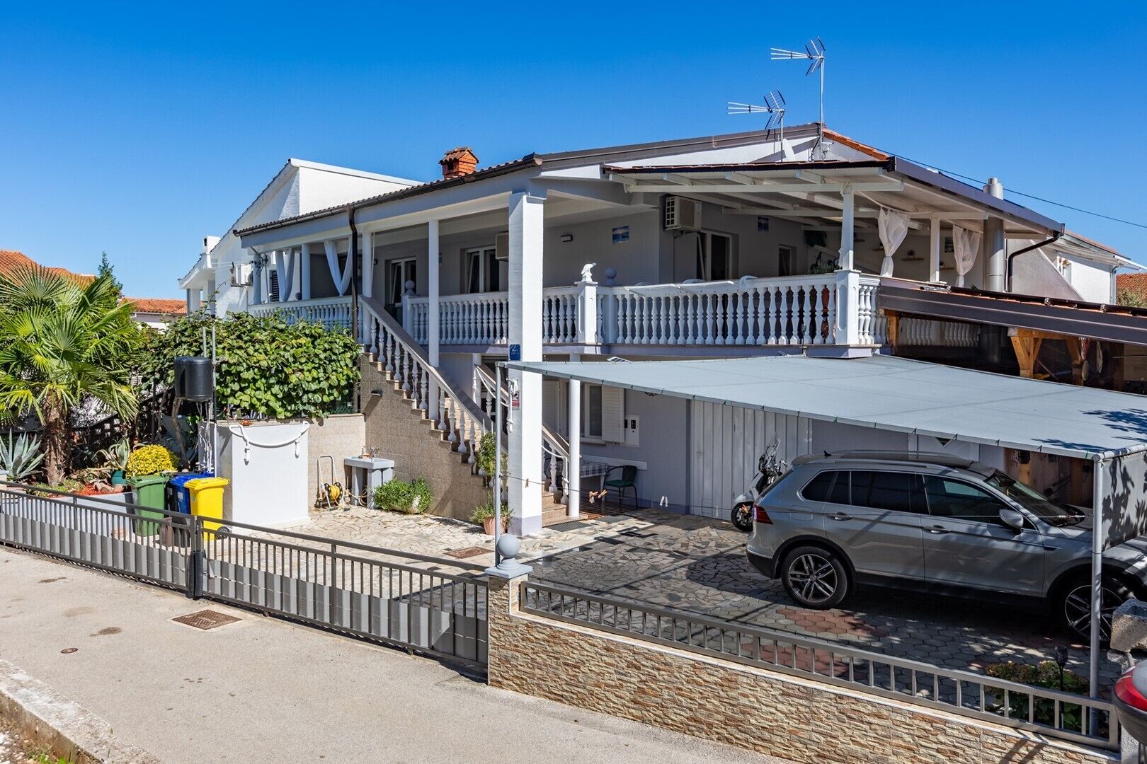 Une maison à deux étages avec un porche couvert, un escalier et une voiture garée dans l’allée.