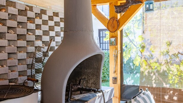 A stone oven with a chimney, a checkered brick wall, and a window with a view of greenery.