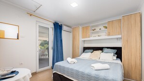 A bedroom with a bed, a table with a bowl and a remote, a blue curtain, and a sliding door to a balcony.