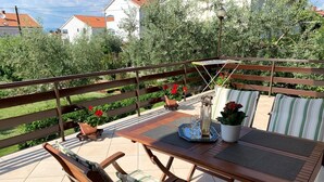 Een terras buiten met een houten tafel, stoelen en potplanten.