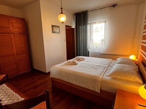 Quarto com cama de madeira, mesa de cabeceira, cadeira, guarda-roupa e luminária suspensa.