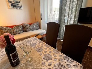 Et spiseområde med et bord dækket til to, en vinflaske og et fjernsyn i baggrunden.