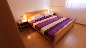 Een opgemaakt bed met een gestreept deken, een bedlampje en een nachtkastje.