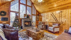 A cozy log cabin interior with a fireplace, leather furniture, and a Christmas tree.