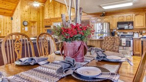 A wooden interior with a dining table set for four, a kitchen area with appliances, and a rustic decor.