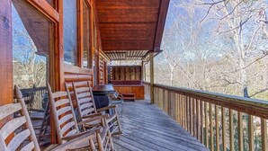 A wooden deck with outdoor seating and a grill, overlooking a forested area.