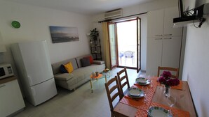 A compact living space with a kitchenette, a sofa, a dining table set for two, and a sliding glass door leading to an outdoor area.
