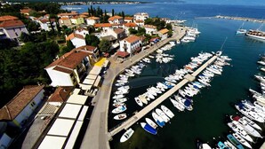 An aerial view of a marina with boats docked along the waterfront, surrounded by residential buildings with red-tiled roofs.