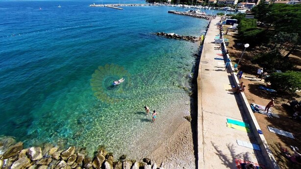 A coastal beach with clear water, a rocky shoreline, and a pier extending into the sea.