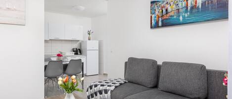 A modern living room with a grey sofa, a wooden coffee table with a vase of flowers, and a painting of a cityscape on the wall.