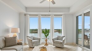 Ein geräumiges Wohnzimmer mit großem Fenster, zwei Sesseln, einem Couchtisch mit Dekoration und einem Deckenventilator.