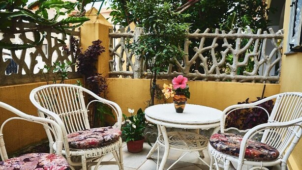 A patio area with wicker chairs and a round table, surrounded by potted plants and a decorative fence. - Appartamento Iris 2- IUN P2186 Rose (Cala Gonone)