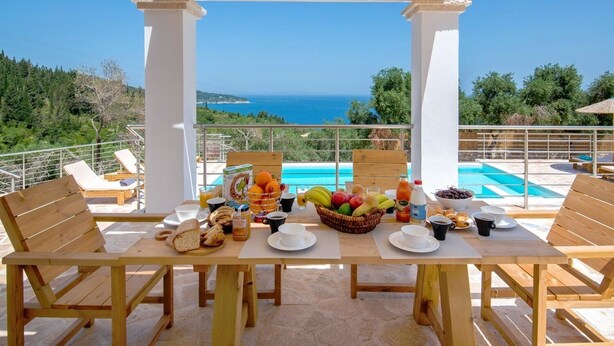 A wooden table set with breakfast items and a view of the sea. - Vasiliki Villa - Four Bedroom Villa, Sleeps 8 (Gaios)