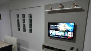 A living room with a mounted TV, a white sofa, a dining table, and a white wall with decorative items.