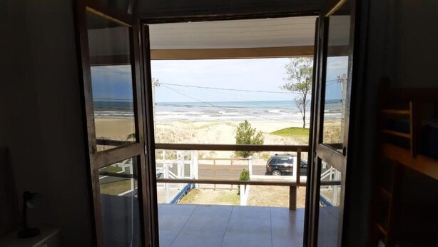 A room with a large sliding glass door leading to a balcony overlooking a beach.