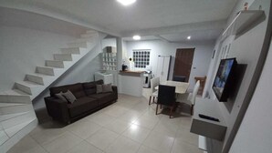 A compact living space with a staircase, a sofa, a dining table, and a TV.