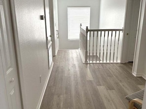 Un couloir doté d’un plancher en bois, de murs blancs et d’une rambarde blanche.