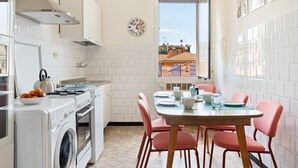 A compact kitchen with a washing machine, a stove, and a dining area with pink chairs and a table. - San Donato Bologna Fiere Apartment (Bologna)
