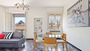 A modern living room with a grey sofa, wooden chairs, a glass table, and a large window with curtains. - San Donato Bologna Fiere Apartment (Bologna)