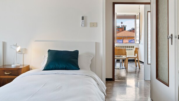 A hotel room with a bed, bedside table, lamp, and a view of the outside balcony. - San Donato Bologna Fiere Apartment (Bologna)