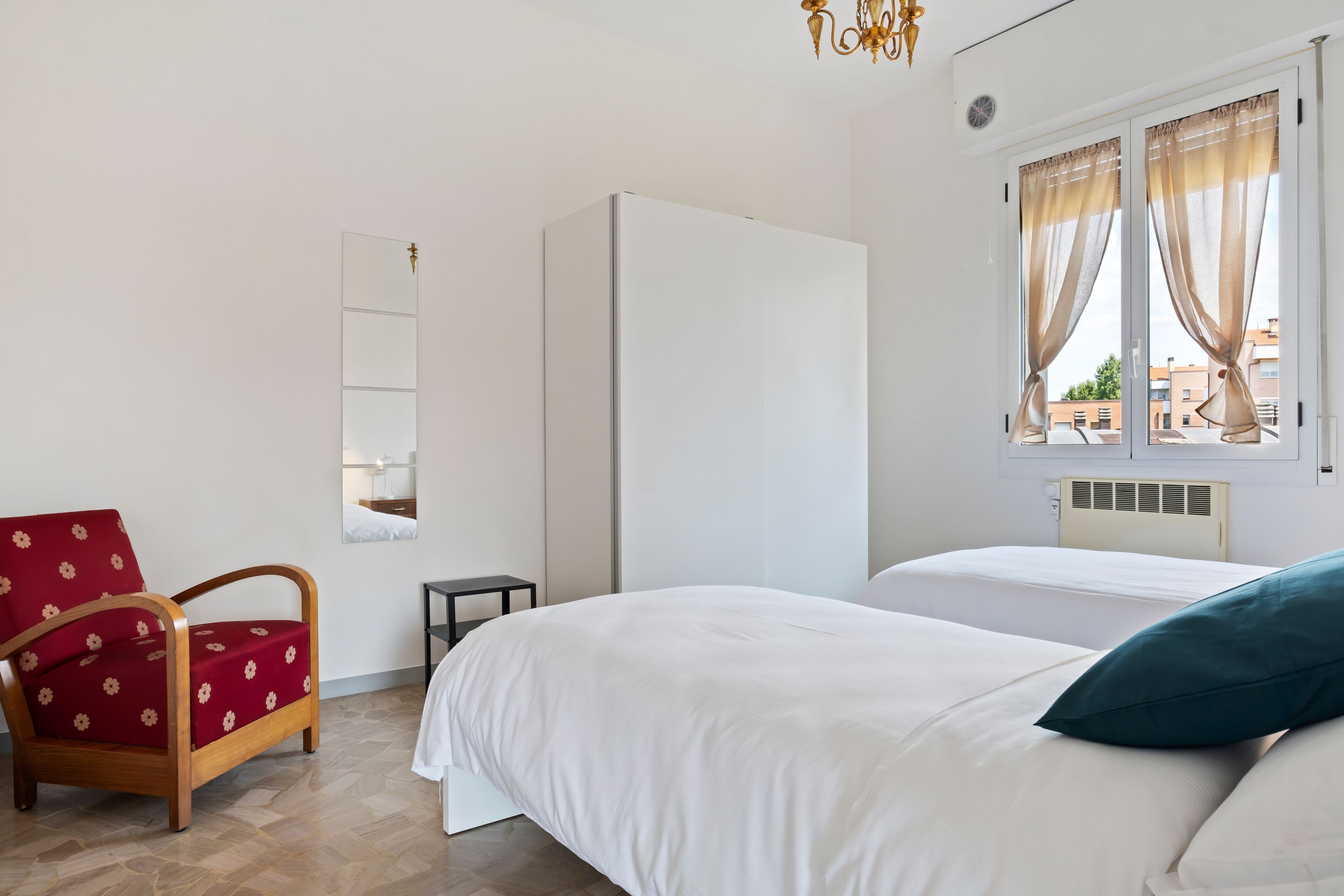 Quarto com duas camas, uma cadeira, um guarda-roupa e uma janela com cortinas.