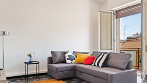 A modern living room with a grey sectional sofa, a small side table with a vase, and a large orange rug. - San Donato Bologna Fiere Apartment (Bologna)