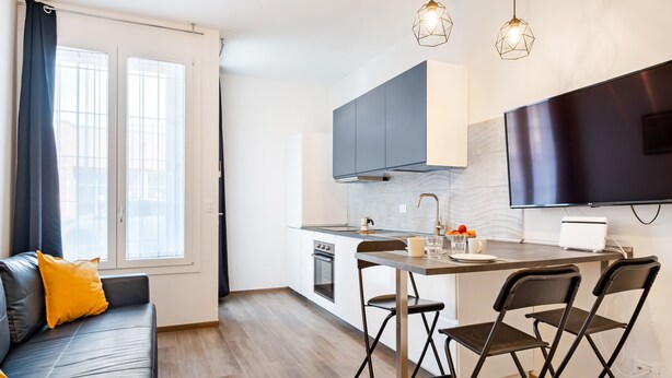 Una cocina moderna con comedor, un sofá con cojines amarillos y un televisor montado en la pared.